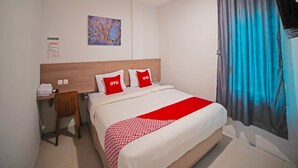 Habitación de hotel con cama, escritorio, silla, televisor de pared y ventana con cortinas.