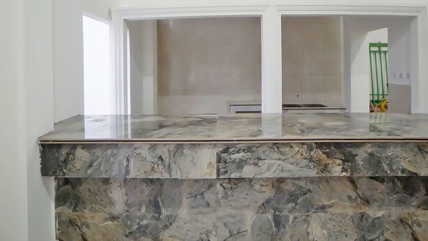 Una habitación con encimera de mármol, paredes blancas y una verja de metal verde al fondo.