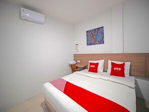 A hotel room with a bed, a nightstand, a wall-mounted air conditioner, and a painting. - Hotel O Saudara Residence (Medan)