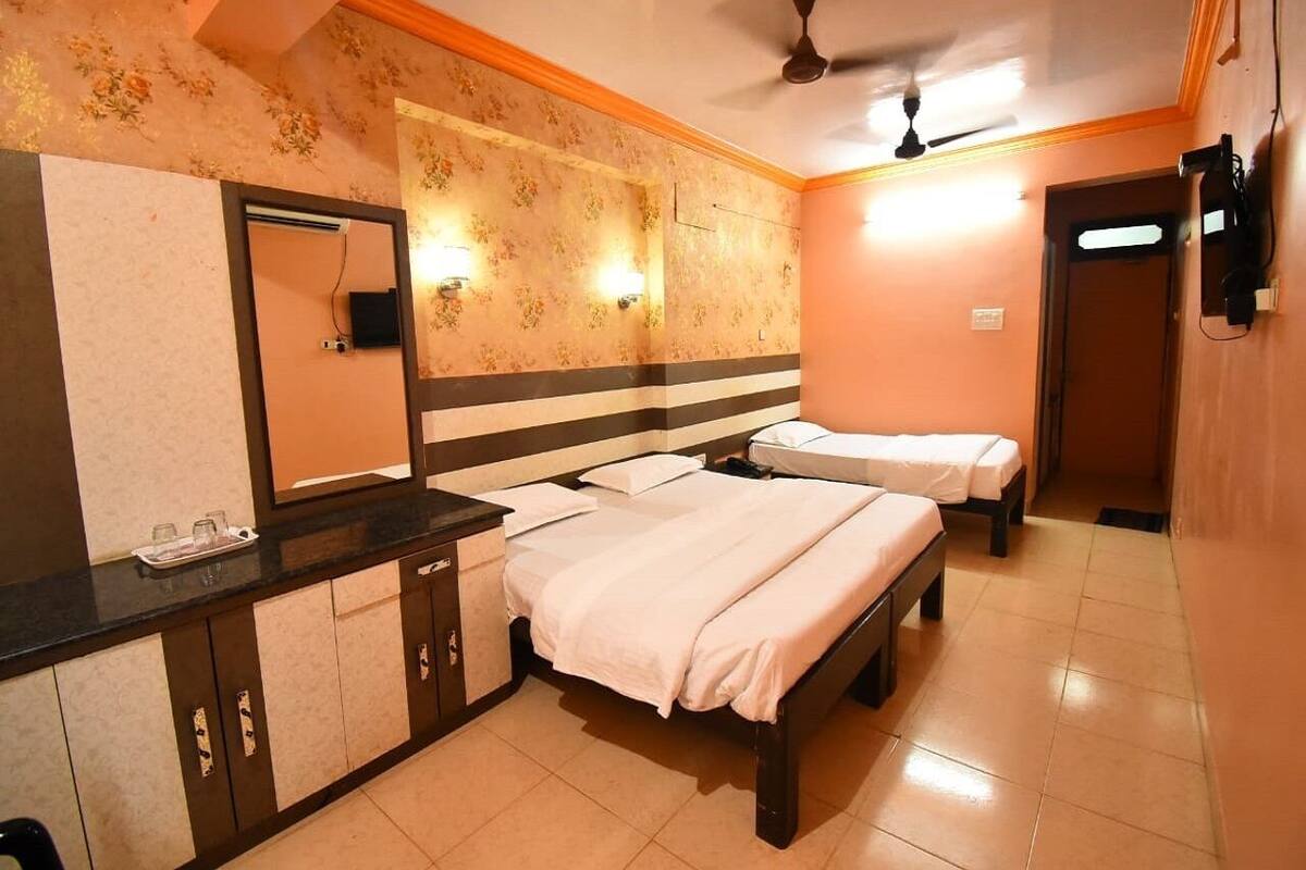 Una habitación de hotel con dos camas, un espejo grande, un tocador con lavabo y un ventilador de techo.