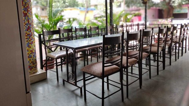 An outdoor dining area with multiple tables and chairs, surrounded by glass walls and a tiled floor. - Hotel Shell Top  (Panaji)