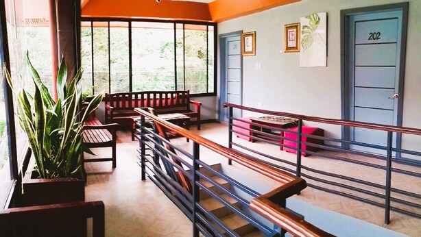 A spacious lobby with a wooden bench seating area, a staircase with metal railings, and a door labeled "202". - Felli's Guest House  (Tagbilaran)