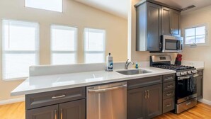 A modern kitchen with a large island, stainless steel appliances, and a window with blinds. - Serene Point Loma Retreat - Modern 2BR with Views of Point Loma (San Diego)