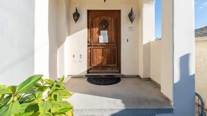 A wooden door with a sign, two wall-mounted lights, and a concrete entrance area. - Serene Point Loma Retreat - Modern 2BR with Views of Point Loma (San Diego)