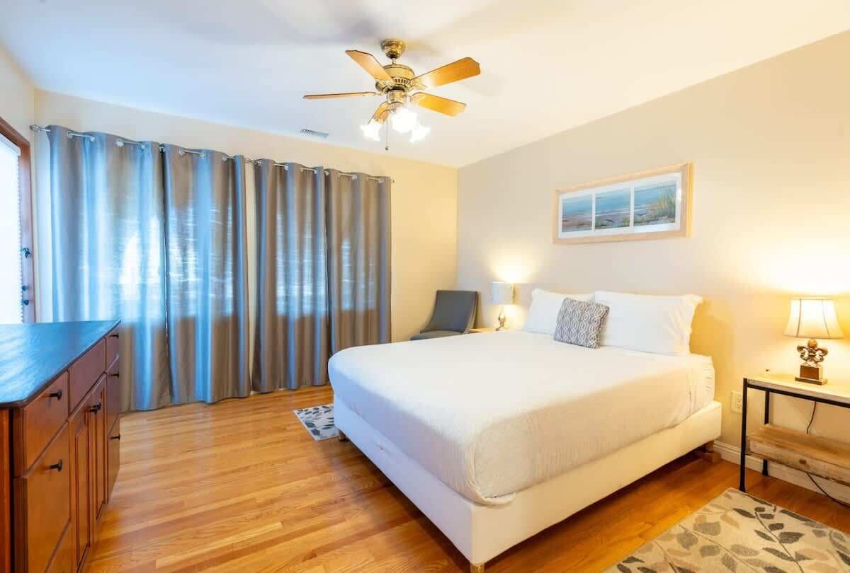 A bedroom with a bed, a desk, a chair, a ceiling fan, and curtains.