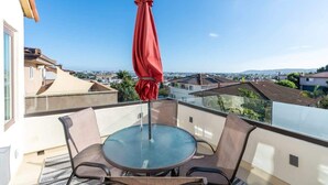 A balcony with a round table and chairs, a red umbrella, and a city view. - Serene Point Loma Retreat - Modern 2BR with Views of Point Loma (San Diego)