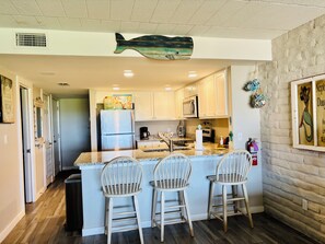 Une cuisine avec un îlot central, des chaises en bois, un réfrigérateur, un four à micro-ondes et un motif décoratif représentant un poisson au plafond.