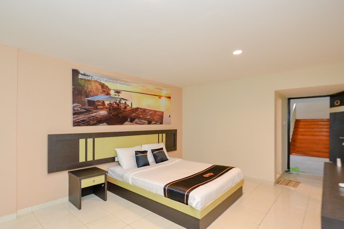 A hotel room with a bed, a nightstand, a poster on the wall, and a door to the right.