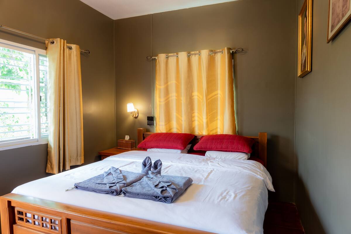 Quarto de hotel com cama, cortinas, mesa de cabeceira, luminária e janela.
