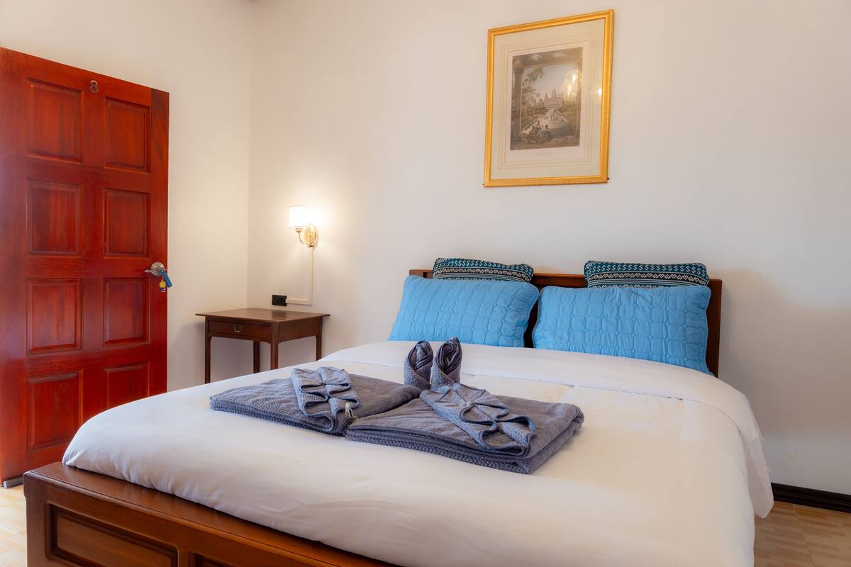 Cama bem arrumada com almofadas azuis e um quadro na parede.