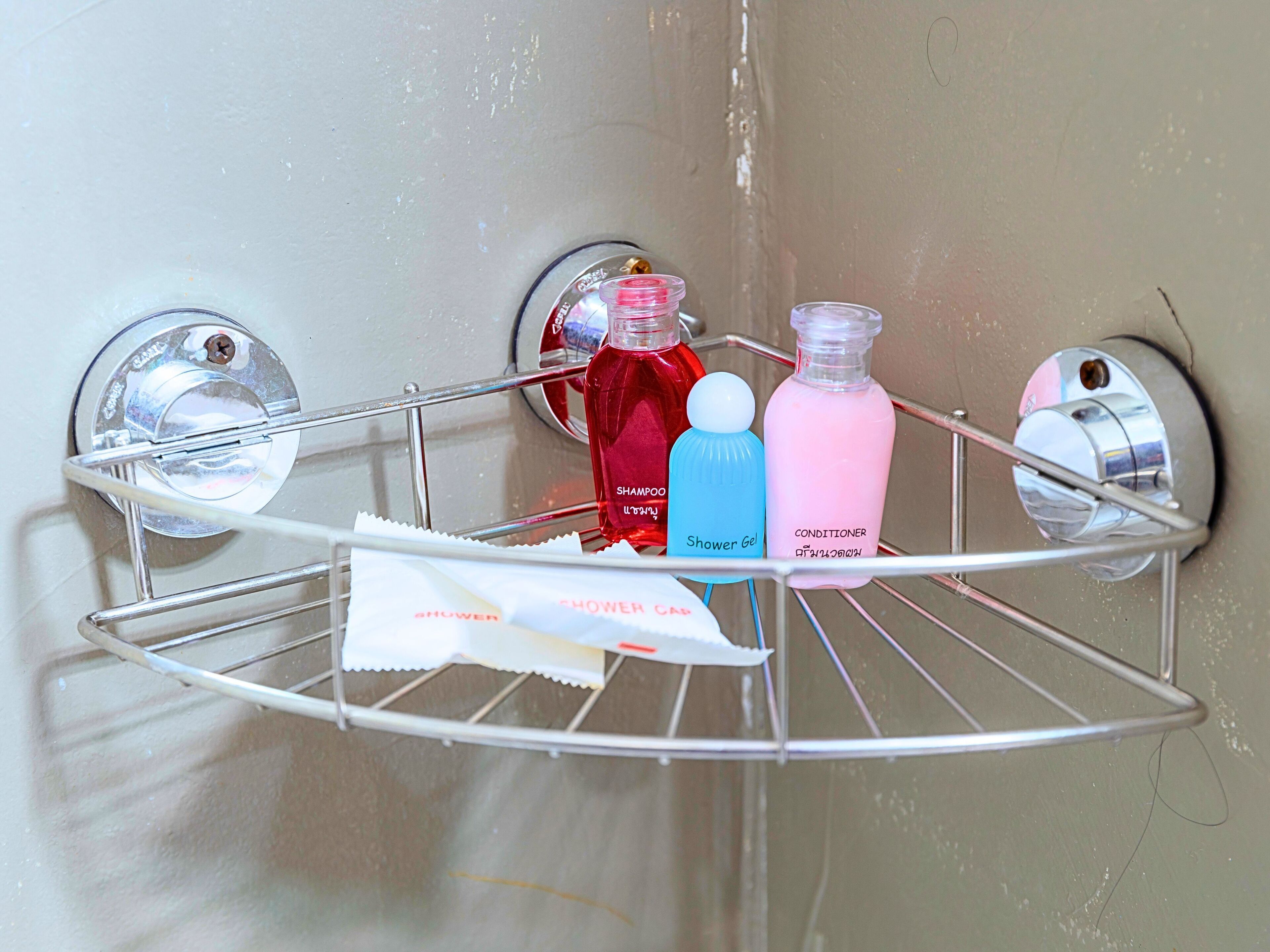A bathroom corner with a chrome towel rack holding a shower gel bottle, a shampoo bottle, and a conditioner bottle.