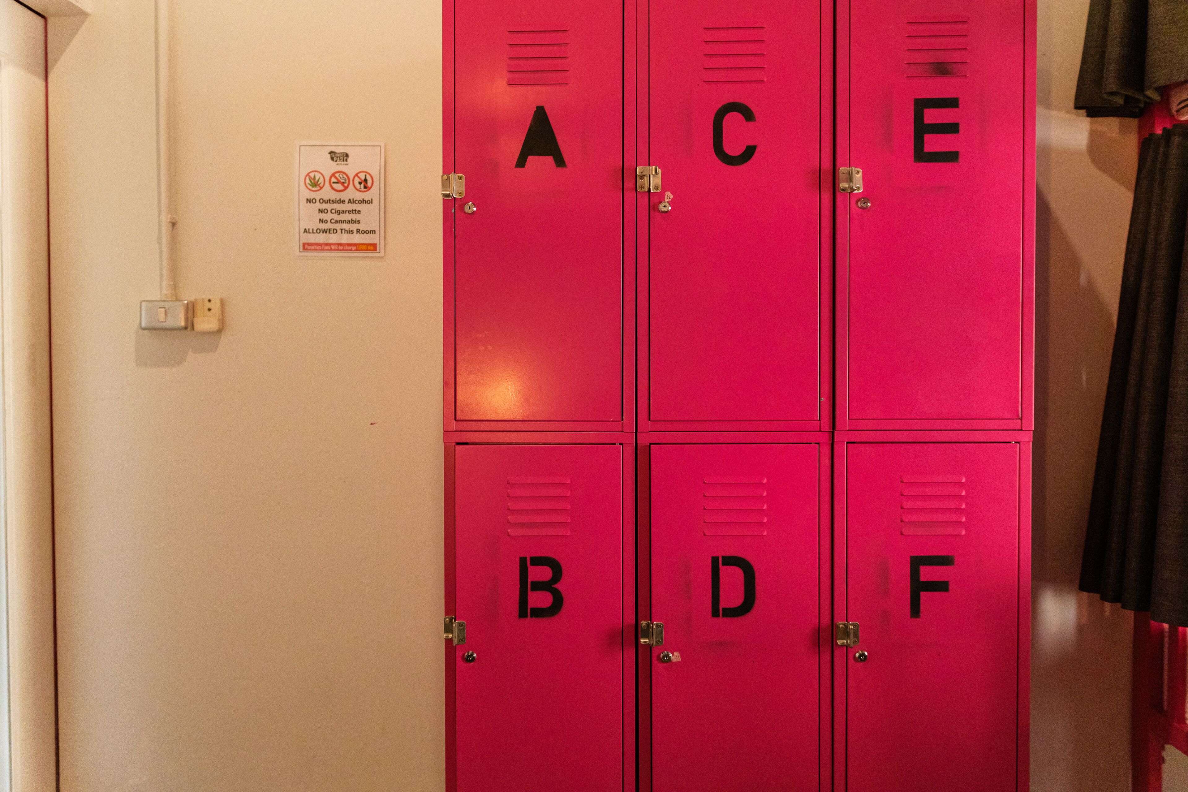A set of six red lockers labeled A to F, with a no smoking, no outside alcohol, and no smoking allowed sign on the wall.