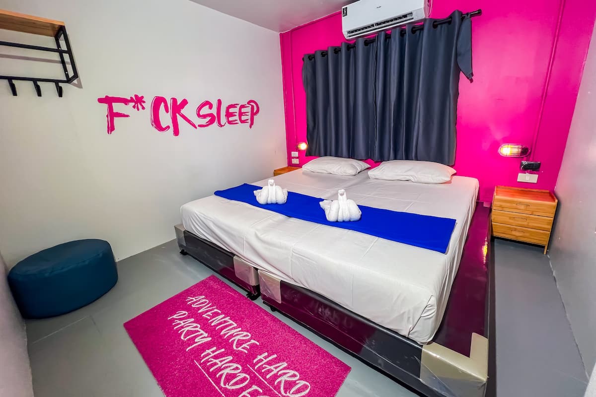 Un dormitorio moderno con cama, mesita de noche, aire acondicionado instalado en la pared y una pared rosa brillante con un mensaje motivacional.