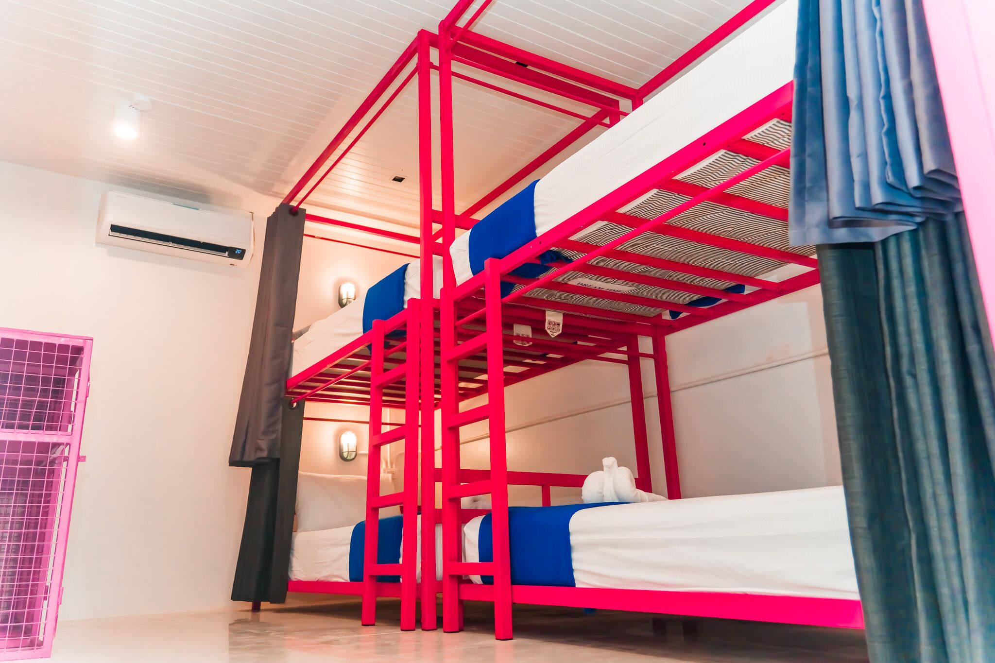 Camera con letto a castello dalla struttura rossa, soffitto bianco e finestra con tende.