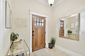 Un couloir avec une porte en bois, un grand miroir et une vitrine contenant des fleurs.