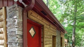 Eine Blockhütte mit roter Tür, Steinmauern und einem steinernen Weg, der zum Eingang führt.