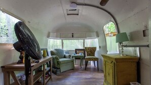 Ein gemütlicher, kompakter Innenraum mit einem Holztisch, einem grünen Sessel, einem Sessel mit Leopardenmuster und einem Vintage-Schrank.