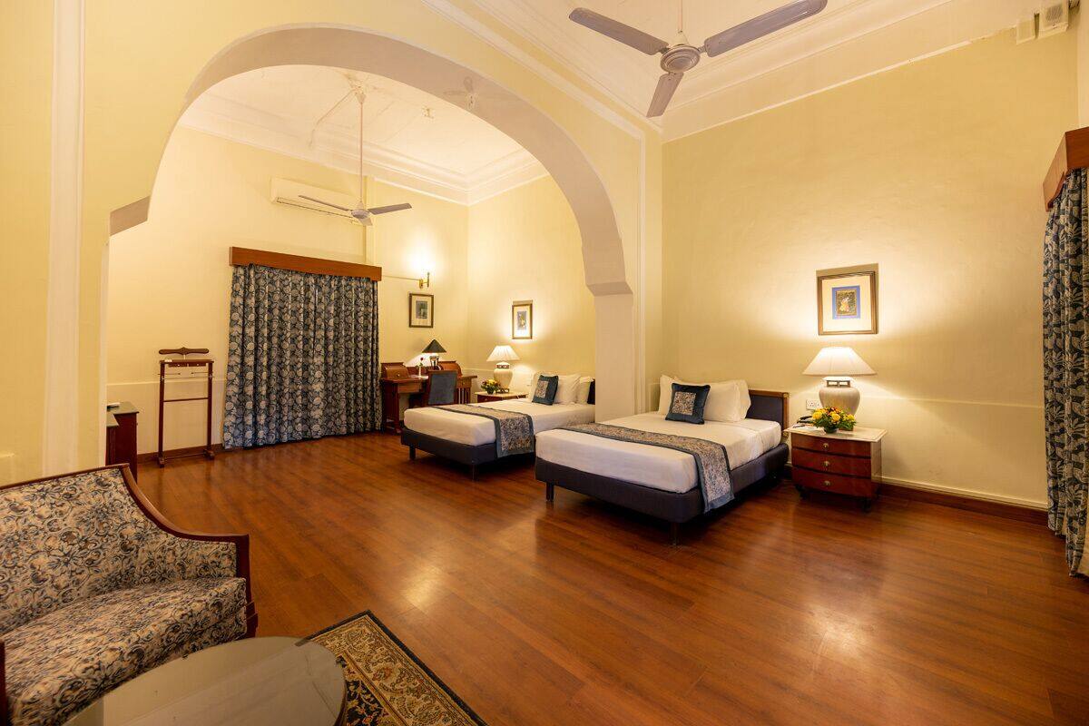 Quarto de hotel com duas camas, uma escrivaninha, uma cadeira e um sofá.