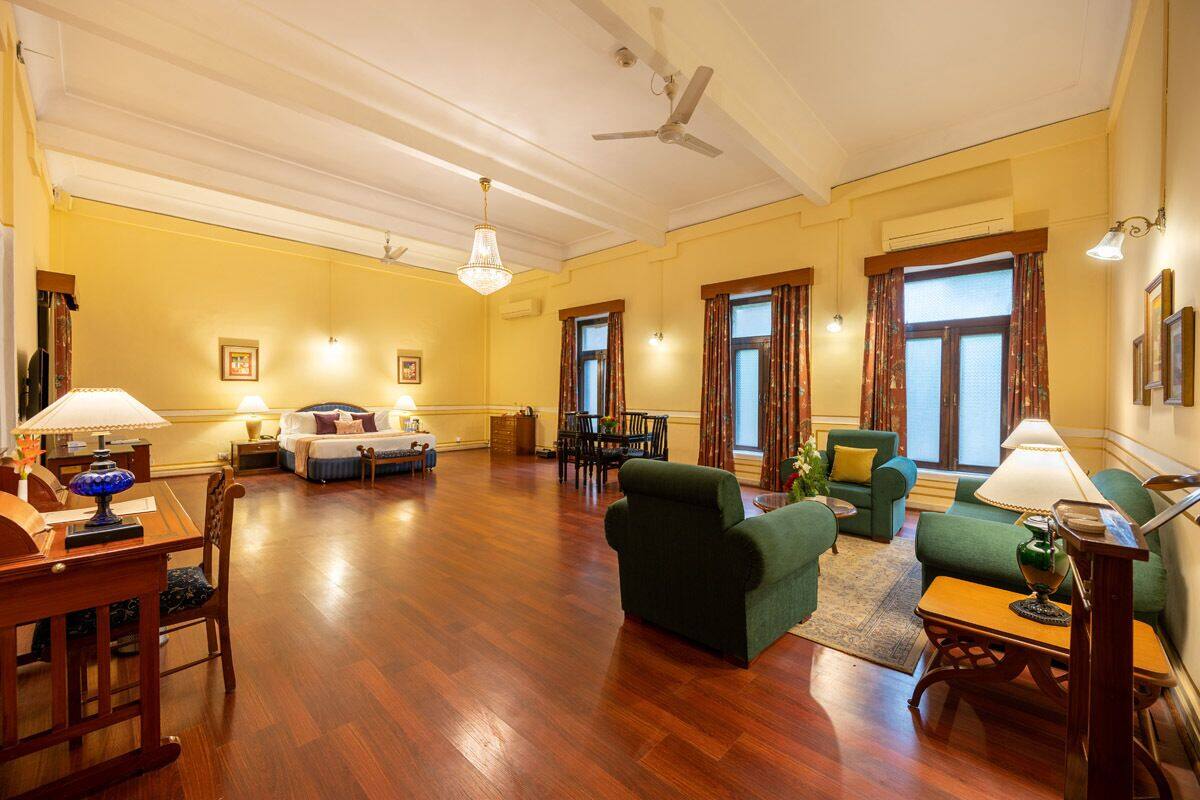 Uma sala de estar espaçosa com piso de madeira, poltronas verdes, um sofá, uma mesa de jantar com cadeiras e um ventilador de teto.