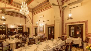 A dining area with multiple tables set for service, chandeliers, and ornate ceiling designs. - Umed Bhawan Palace (Kota)