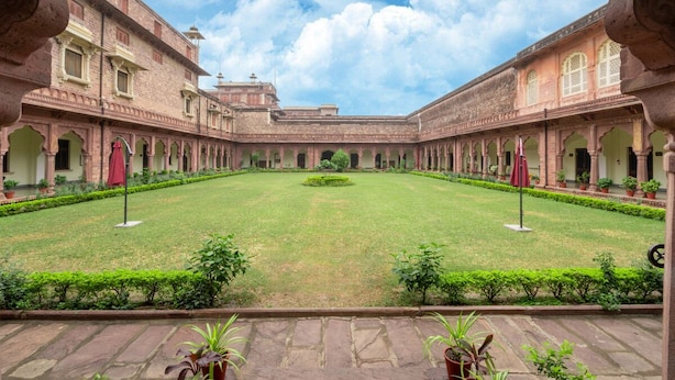 A courtyard with a central lawn, surrounded by brick buildings with arched doorways and windows. - Umed Bhawan Palace (Kota)