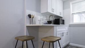 A compact kitchen with white cabinets, a microwave, and two wooden stools. - The Bradley Studio · Near Mystic, Casinos + USCGA (Groton)