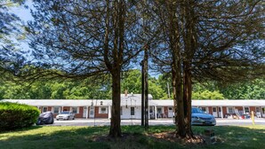 A motel with a row of rooms, covered parking, and a grassy area with trees. - The Bradley Studio · Near Mystic, Casinos + USCGA (Groton)