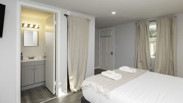 A bedroom with a bed, a bathroom with a sink and mirror, and a door leading to another room. - The Bradley Studio · Near Mystic, Casinos + USCGA (Groton)