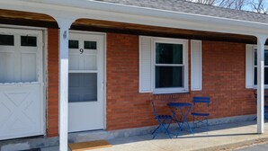A single-story building with a red brick facade, white doors, and shutters, featuring a small porch with blue folding chairs. - The Pratt Studio · Near Mystic, Casinos + USCGA (Groton)