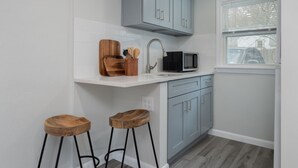 Een compacte keuken met witte tegels, grijze kastjes, een magnetron en twee houten krukken.