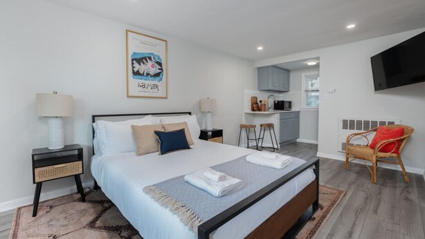 Een moderne hotelkamer met een groot bed, een bureau, een stoel en een kitchenette op de achtergrond.