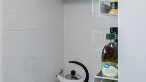 Een keuken met een witte kookplaat, een waterkoker en een fles olijfolie op een plank.