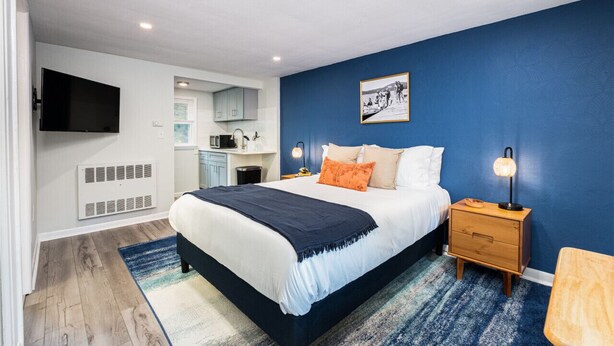 A bedroom with a bed, nightstands, a TV, a microwave, and a small kitchenette.