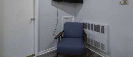 A room with a mounted TV, a chair, a door, and a wall-mounted heater.