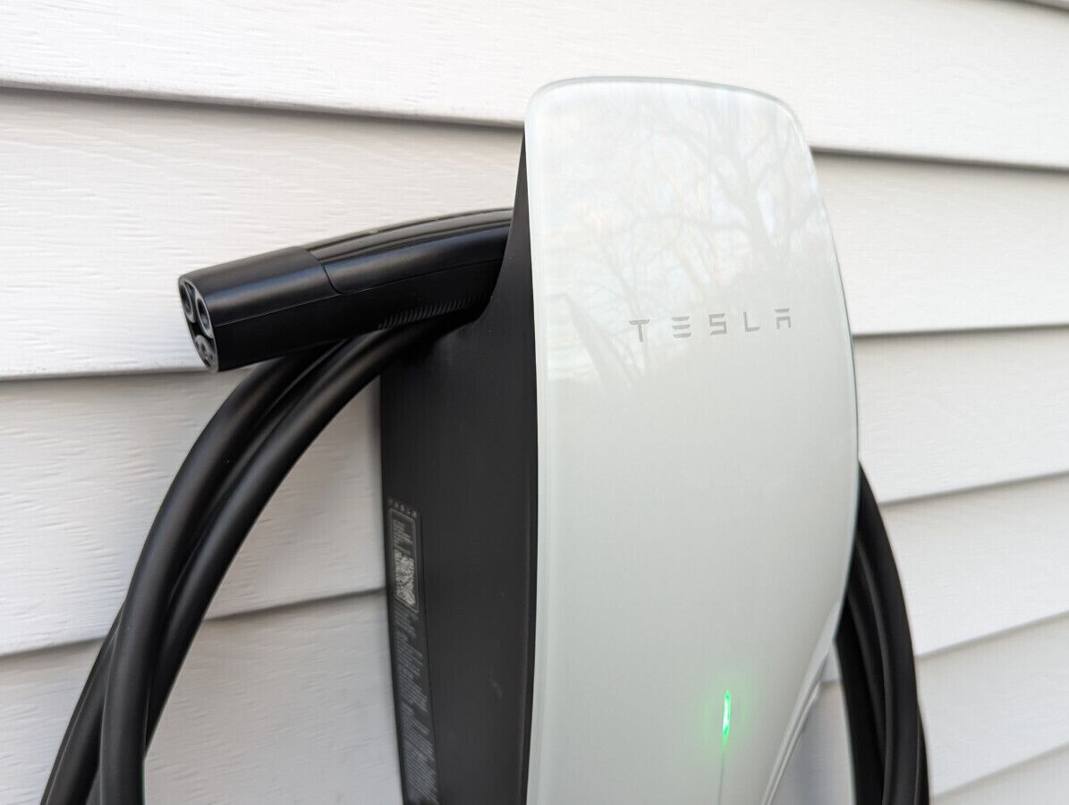 Une borne de recharge Tesla avec un câble noir qui y est connecté.