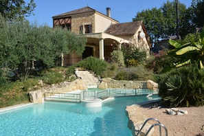 A pool with a stone deck, surrounded by greenery and a stone wall.
