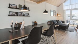 Una sala de estar moderna con comedor, que presenta techo de madera, ventanas amplias y mobiliario contemporáneo.