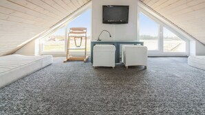 Un dormitorio acogedor en el ático, con techo inclinado, un televisor montado en la pared, una silla de madera y un escritorio pequeño con una lámpara.