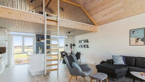 Un interior moderno con un dormitorio tipo loft, una zona de comedor y un salón con sofá y reposapiés.