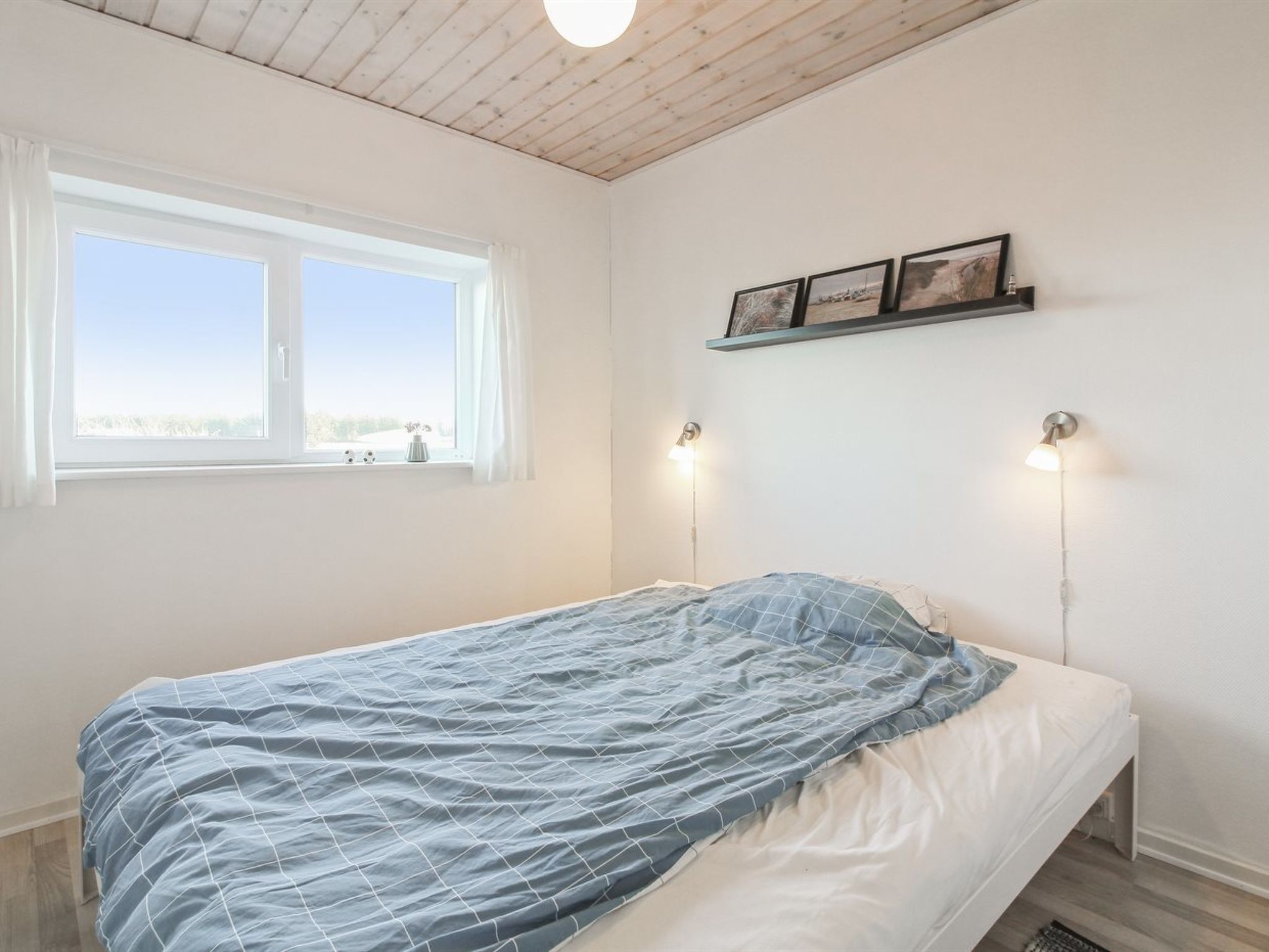Une chambre à coucher avec un lit, une fenêtre et une étagère fixée au mur, sur laquelle sont posées des photos.