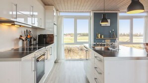 Una cocina moderna con armarios blancos, una isla grande y vistas al campo a través de amplios ventanales.