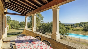 A covered patio with a pool, stone walls, and a view of the countryside.