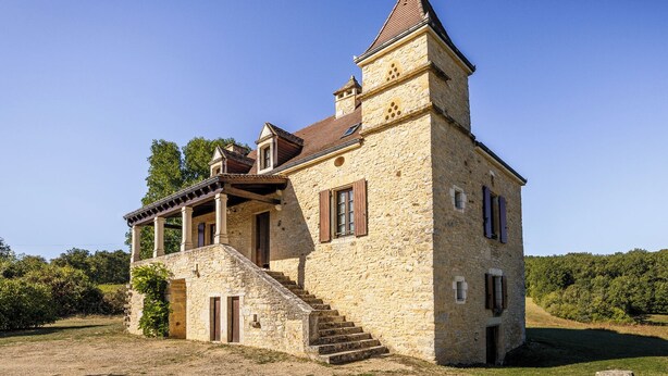 A stone building with a tower, a staircase, and a covered porch.