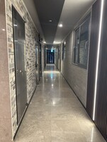 Un pasillo moderno con una pared de ladrillo a un lado y una pared metálica al otro, que conduce a una puerta con la indicación '101'.