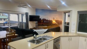 Una cocina moderna con lavavajillas integrado, un comedor con mesa y sillas, y un amplio ventanal con vistas a un paisaje urbano.