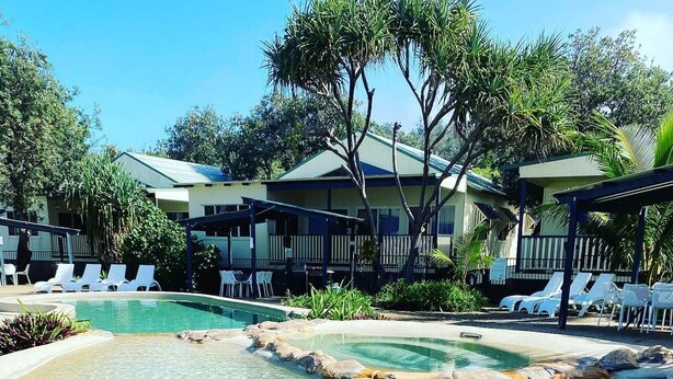 Una piscina cristalina con sillas de descanso y un edificio al fondo.