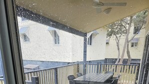 Una terraza de madera con una mesa y sillas, una barandilla de metal y vista a un edificio en el fondo.