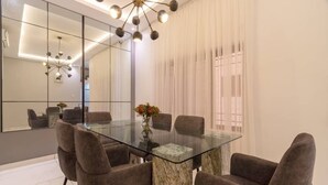 Een moderne eetruimte met een glazen tafel, comfortabele stoelen, een grote spiegel en een moderne kroonluchter.