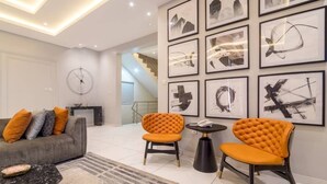 Een moderne woonkamer met een grijze bank, twee oranje fauteuils, een zwarte salontafel en een kamerkleed met een patroon.