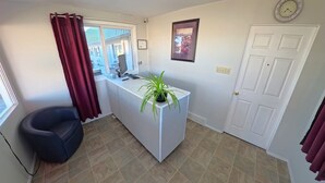 Una habitación pequeña con escritorio, silla, planta en maceta, puerta y ventana con cortinas.